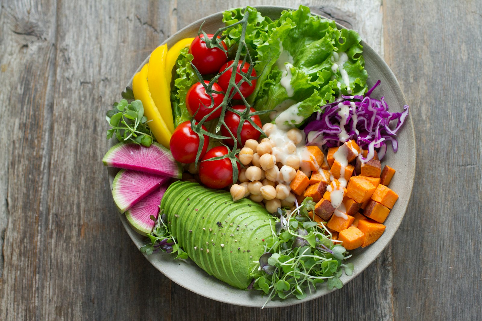 Bowl con ceci, avocado, pomodorini, cavolo viola, patate dolci e ravanelli